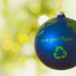 Boule de Noël bleue décorée en forme de planète Terre avec le message 'Love your Planet' et un symbole de recyclage, sur un fond lumineux festif.