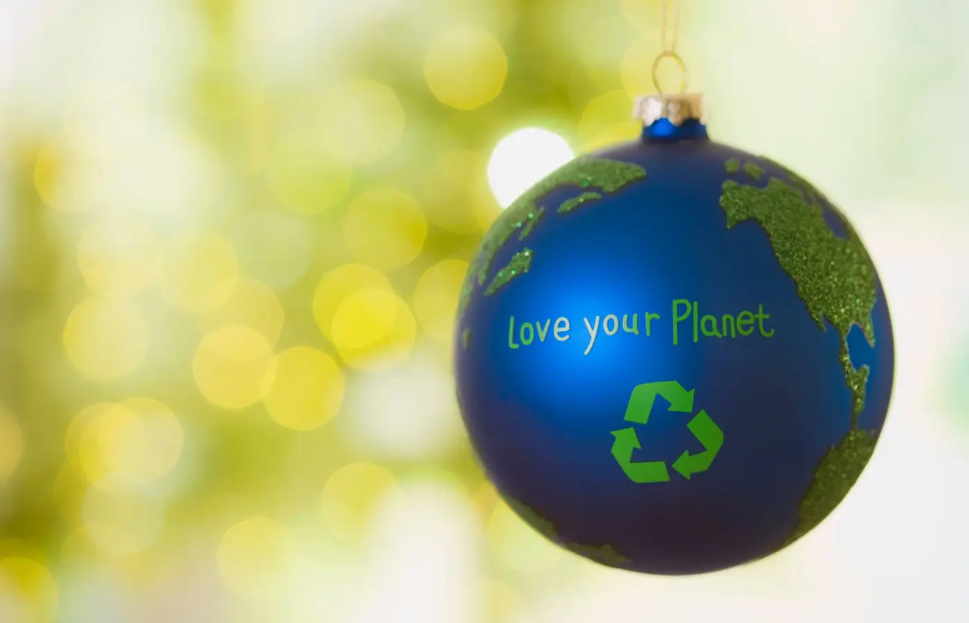 Boule de Noël bleue décorée en forme de planète Terre avec le message 'Love your Planet' et un symbole de recyclage, sur un fond lumineux festif.