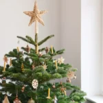 Sapin de Noël naturel décoré avec des ornements écologiques en bois et en paille, surmonté d'une étoile artisanale dans une pièce lumineuse.